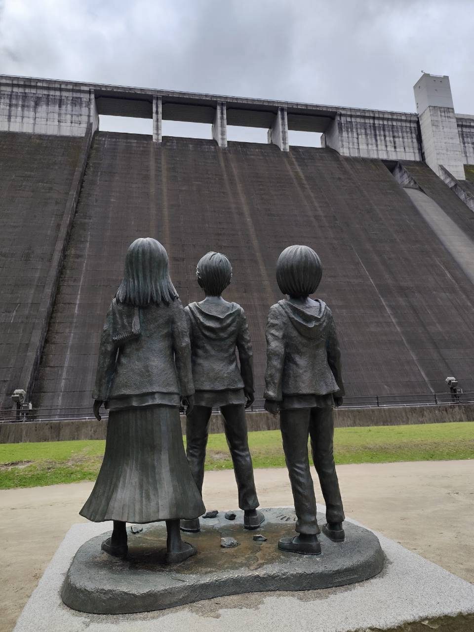Bronze statues of young Eren, Mikasa and Armin looking up at Oyama Dam